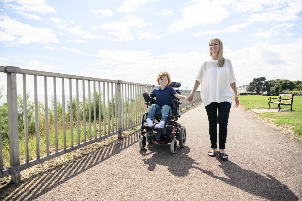 Boy with muscular dystrophy holding hands with his mother as they go down an outdoor path