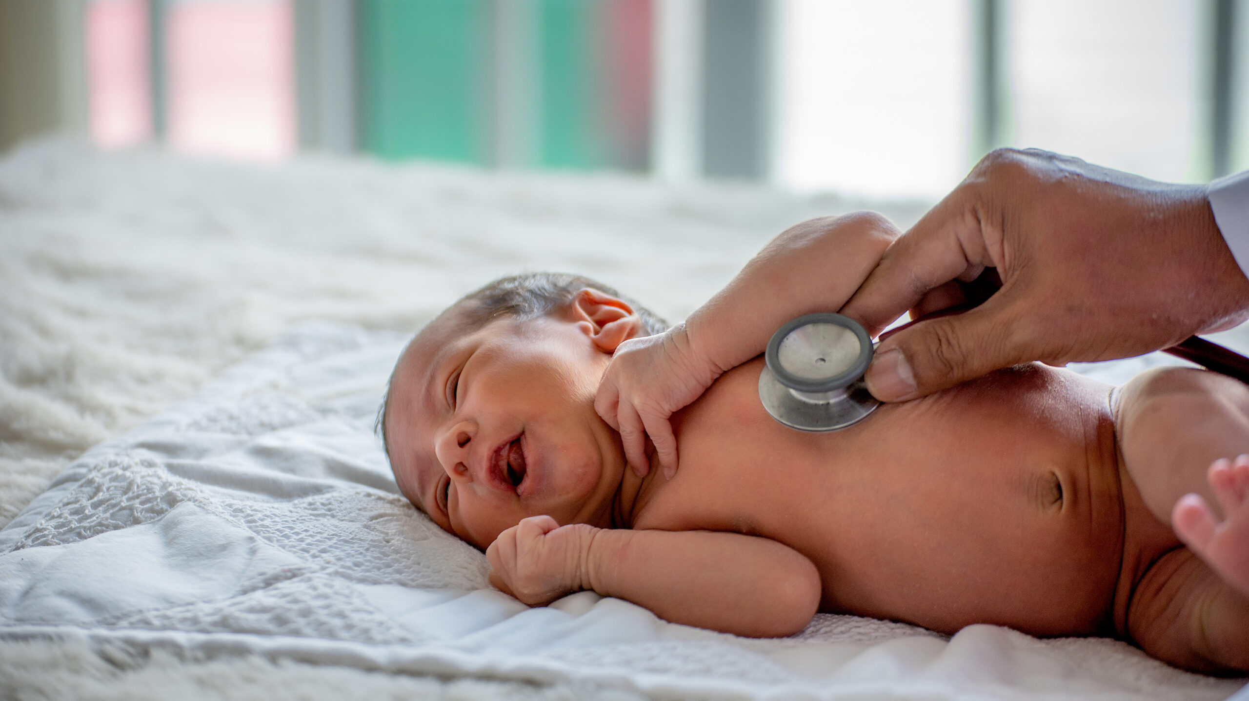 Photo of a newborn baby and a hand holding a stethoscope to their chest